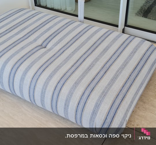 כרית פסים כחולים על רצפת אבן ליד חלון זכוכית.